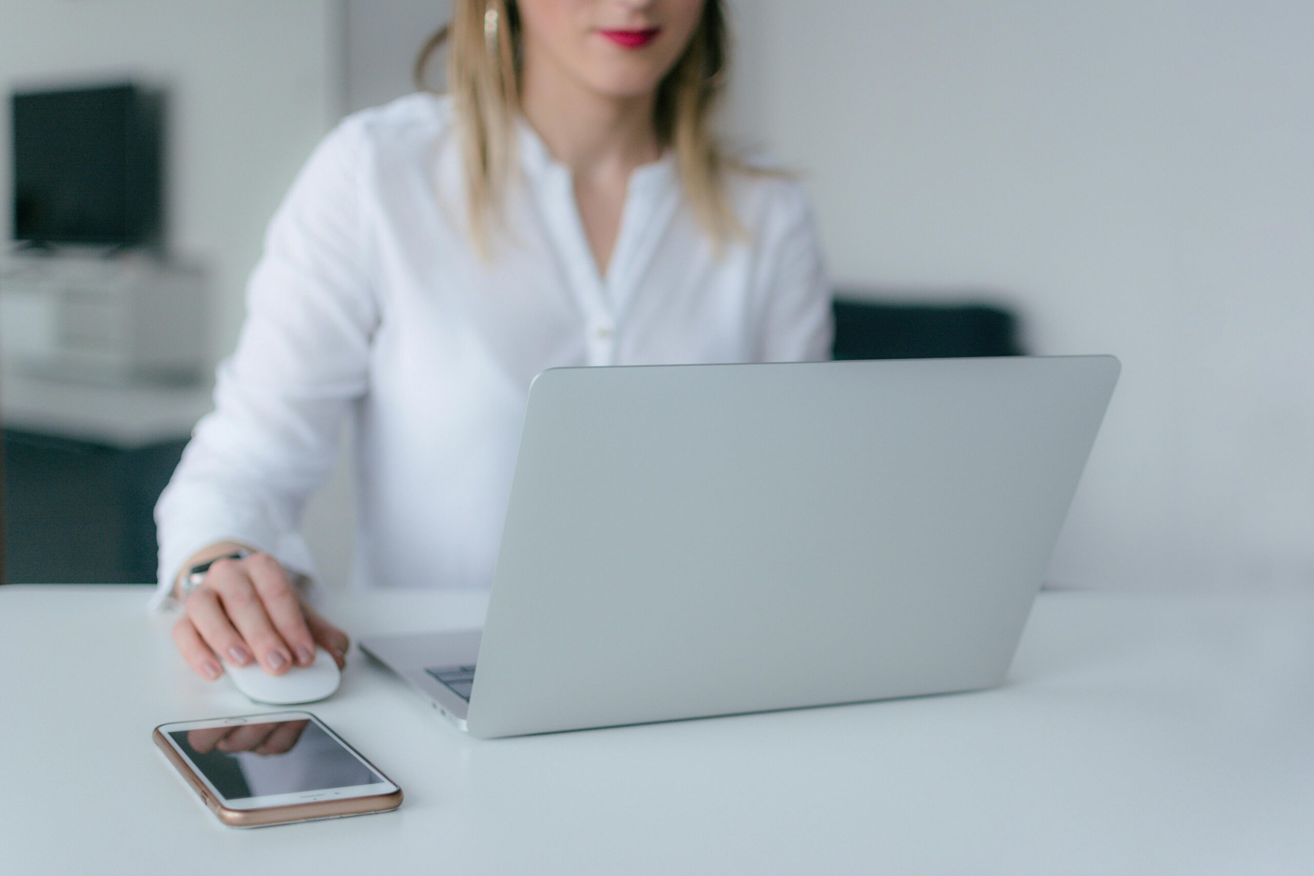 Woman using a laptop and computer mouse at a desk with a smartphone nearby